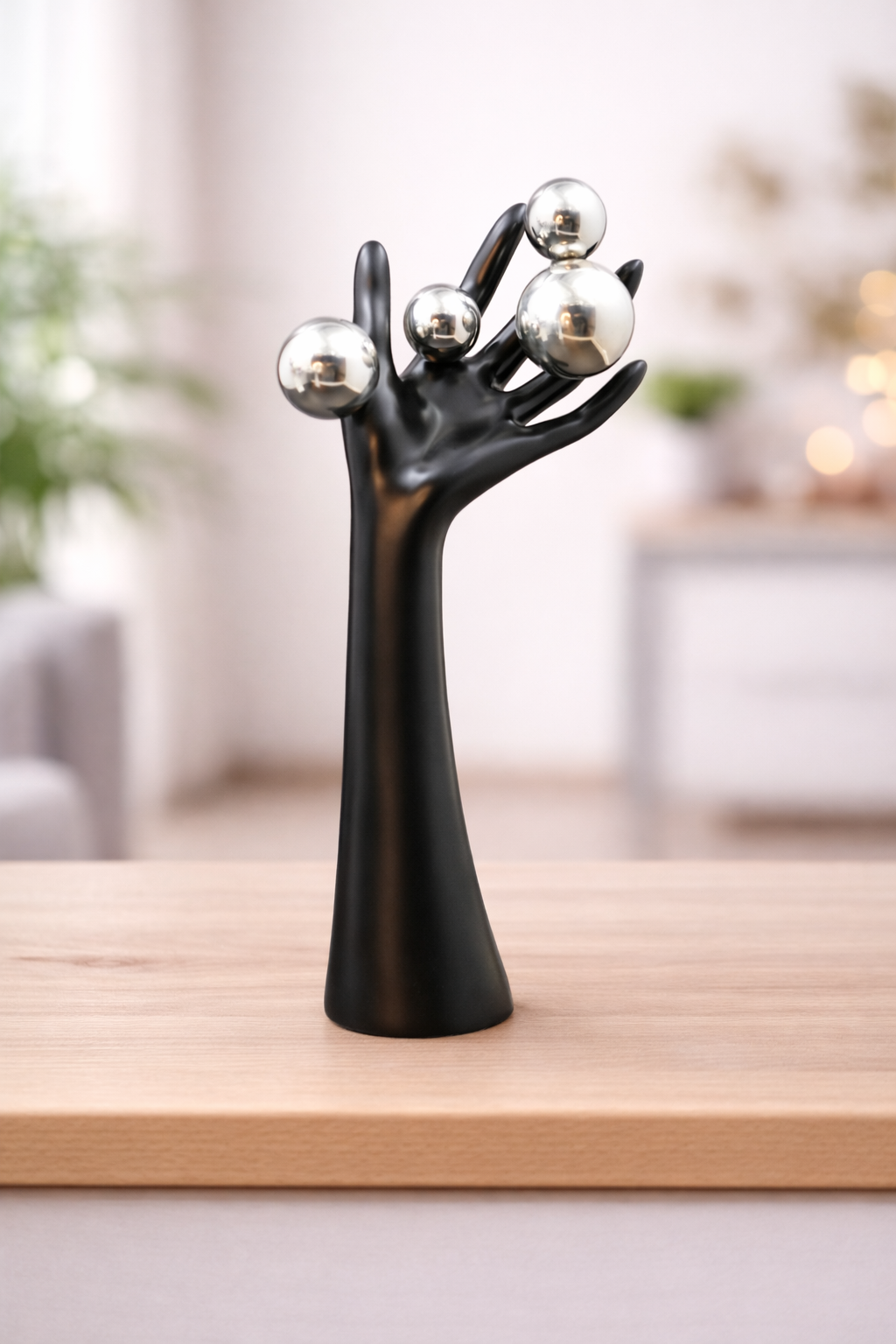 Black decorative sculpture of a hand holding three silver balls.

