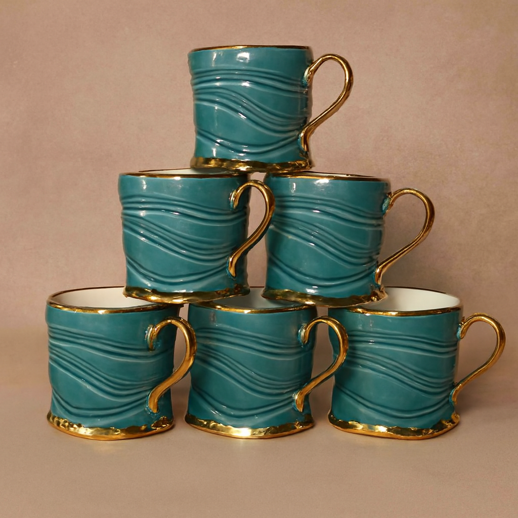 A stack of six mugs with gold handles and rims