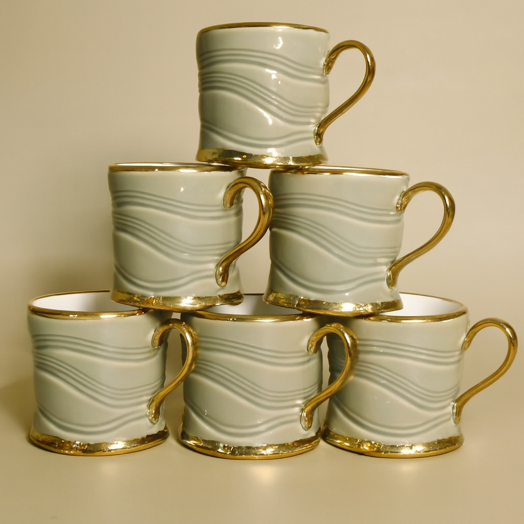 A stack of six mugs with gold handles and rims