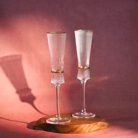 Two ribbed champagne glasses, one filled, on a black table